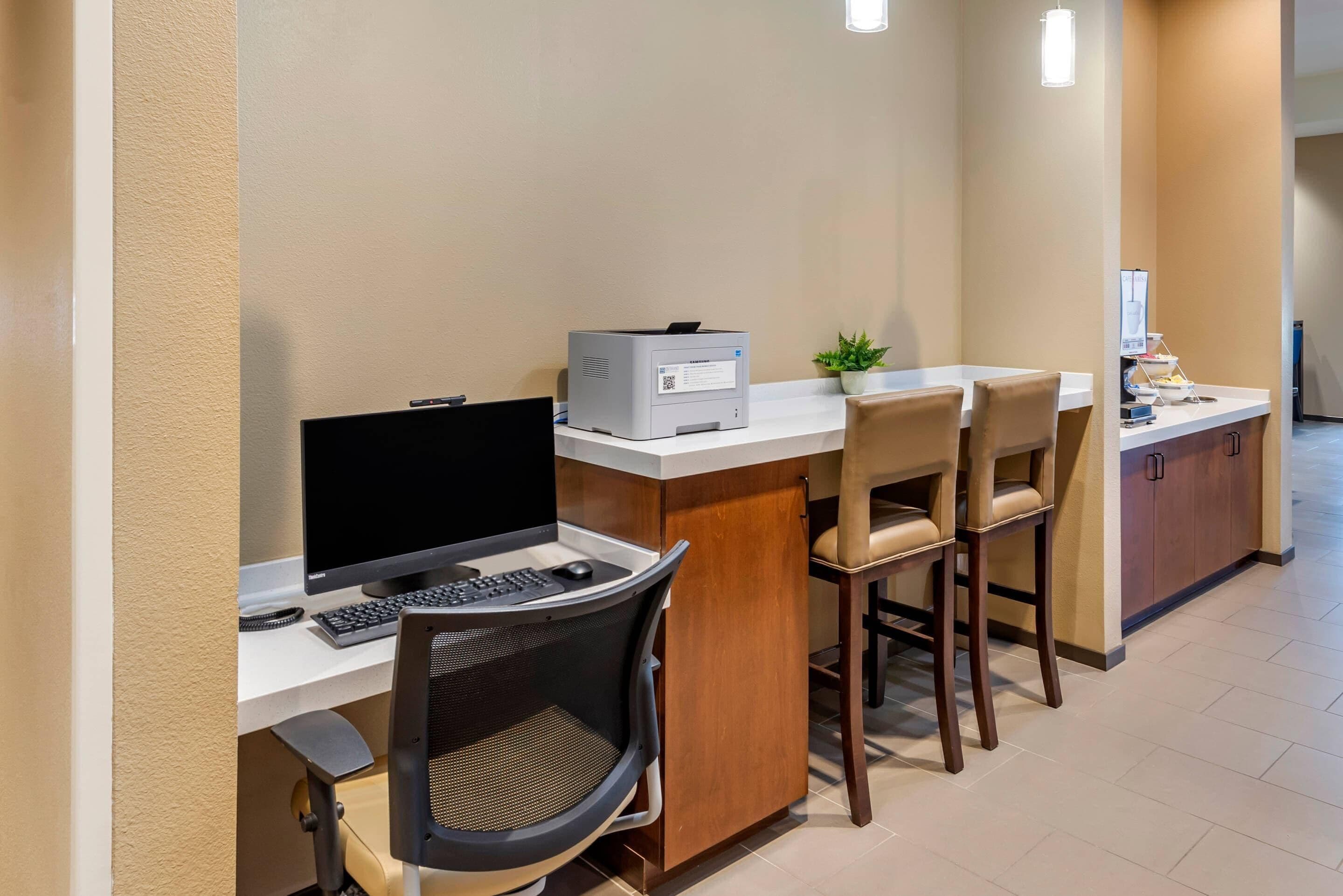 Un espace d’accueil d’hôtel comprenant un bureau avec un ordinateur, des chaises, une imprimante et une petite plante.