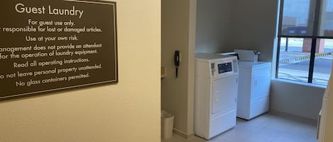 Un espace buanderie à la disposition des clients, avec un panneau indiquant les consignes d’utilisation et offrant une vue sur la pièce.