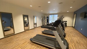Et fitnessrum med løbebånd, et spejl og træningsudstyr.