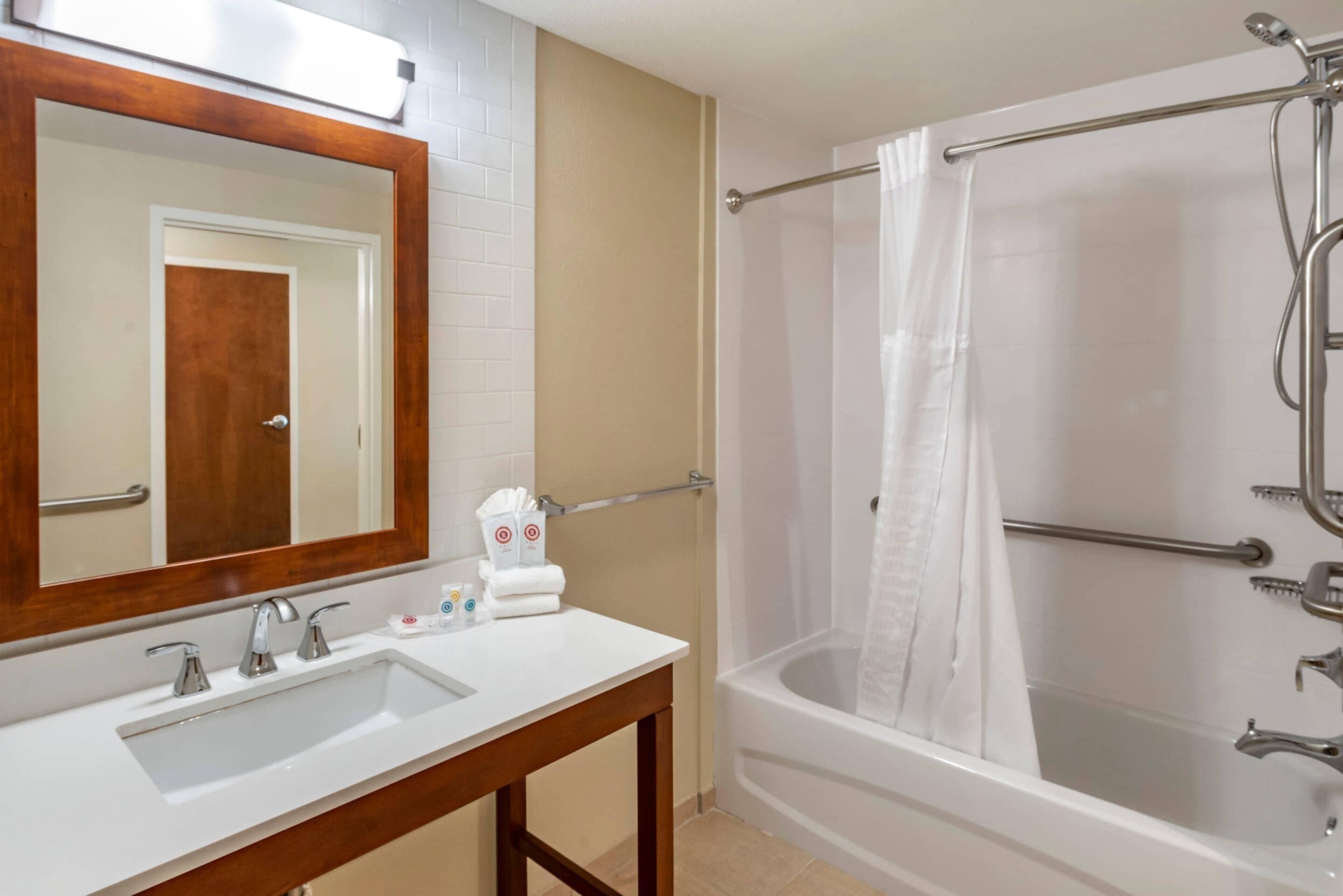 A bathroom with a wooden-framed mirror, a white sink, and a bathtub with a shower curtain.