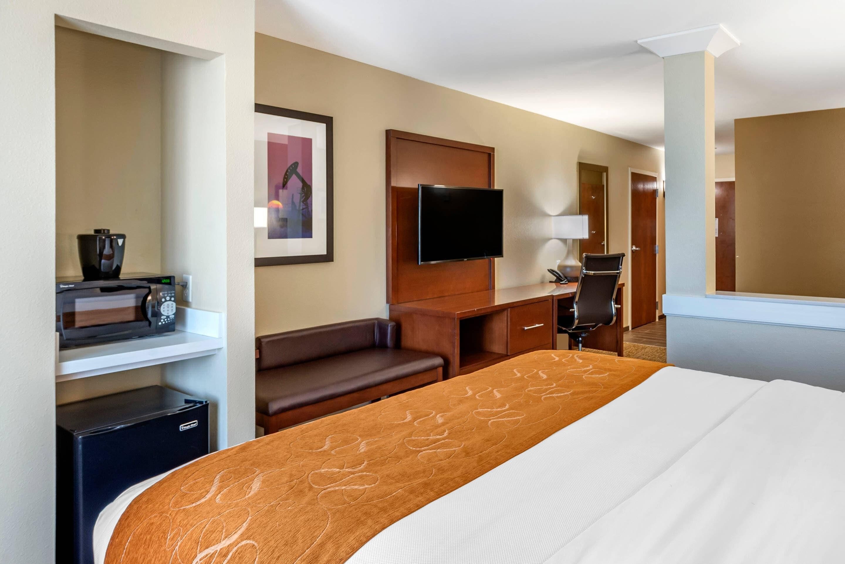 A hotel room with a bed, a desk, a chair, a television, and a small refrigerator.