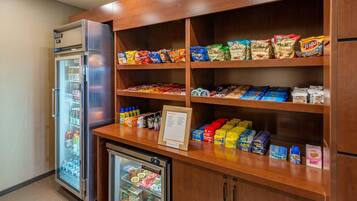 Una kitchenette con refrigerador, mini refrigerador y estantes llenos de botanas y bebidas.