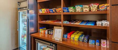 A kitchenette area with a refrigerator, a mini-fridge, and shelves stocked with snacks and beverages.