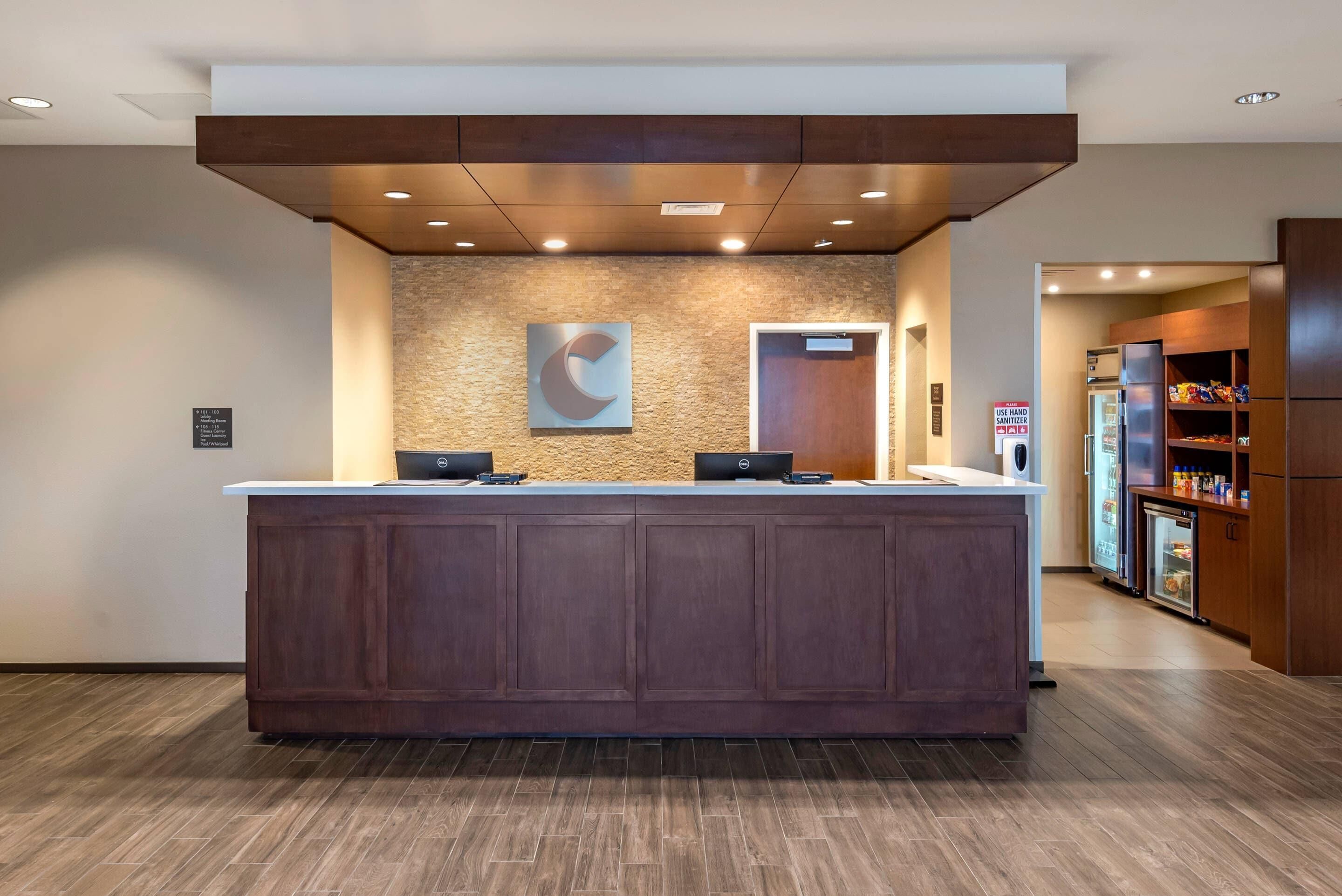 A reception desk with a wooden finish, a stone wall with a logo, and a refrigerator with snacks.