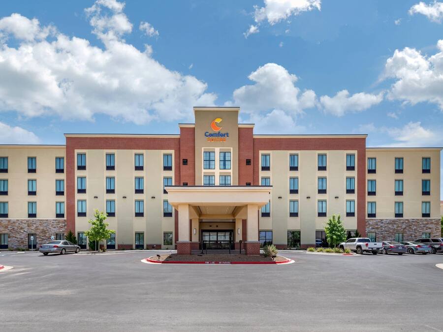 Et Comfort Suites hotel med en central indgang, flere etager og en parkeringsplads.
