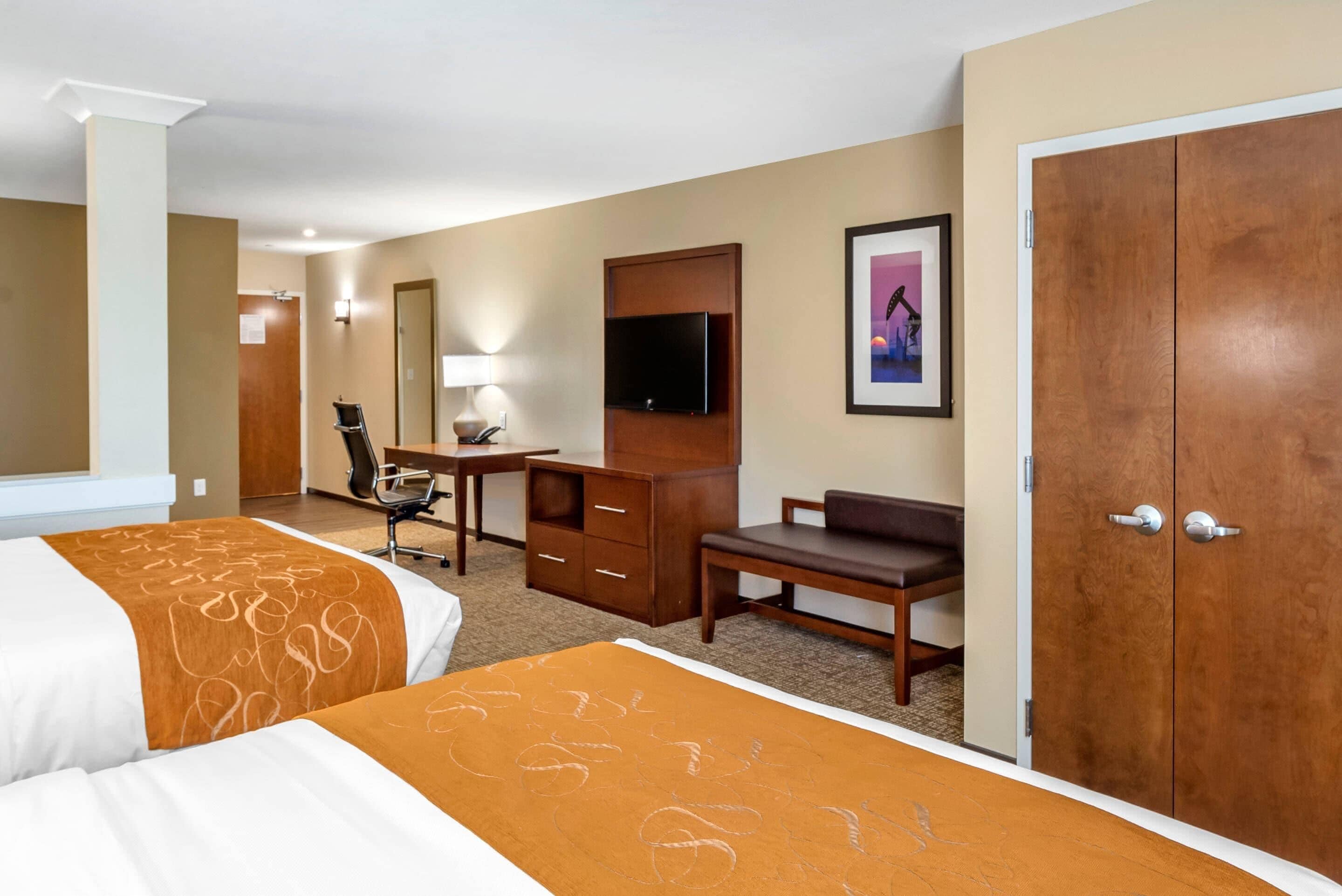 A hotel room with two beds, a desk, a chair, a television, and a door.
