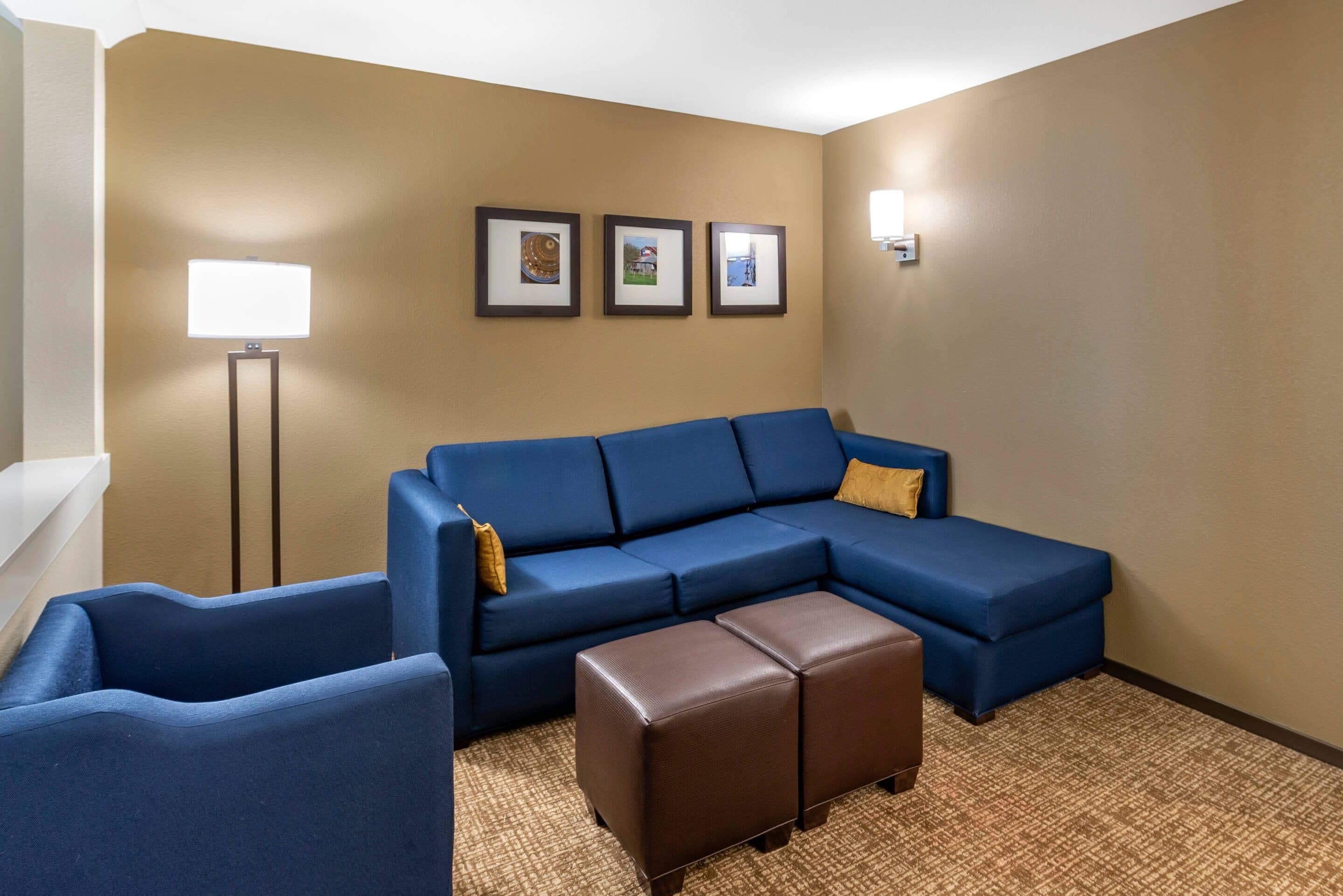 Habitación de hotel con sofá modular, una silla, un pequeño reposapiés, una lámpara de pie y tres cuadros en la pared.