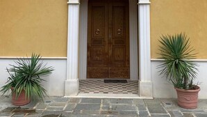 A double wooden door with a checkered floor mat in front, flanked by two potted plants. - Victory House 3 (Celano)