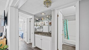 A hallway with a kitchen area featuring white cabinets, a granite countertop, and a glass display cabinet.
