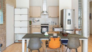 A modern kitchen with white cabinets, a stainless steel refrigerator, and a dining area with two chairs.