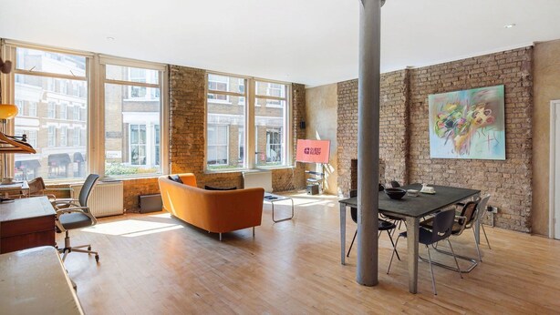 A spacious room with large windows, a brick wall, a modern sofa, a dining table, and a "GUEST READY" sign.