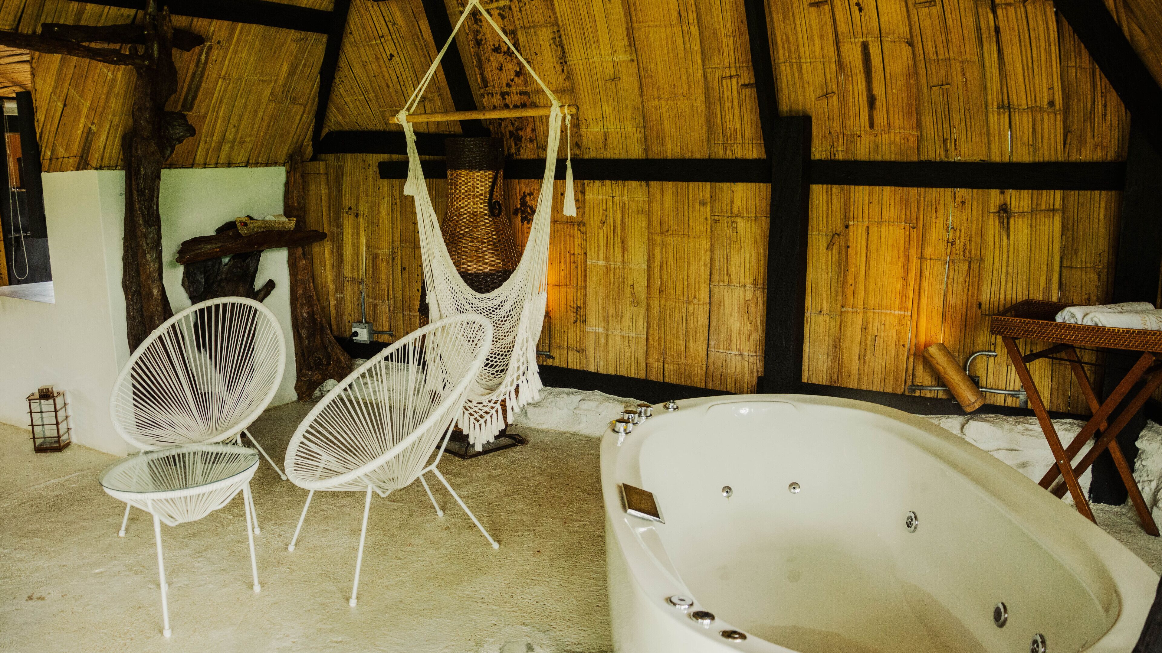 A rustic bathroom with a wooden ceiling, a bathtub, and two white wicker chairs.