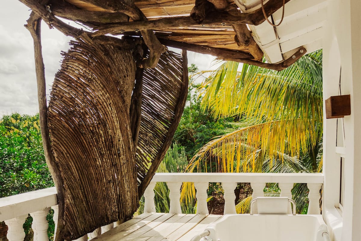 A bathroom with a bathtub, a wooden bench, and a thatched roof structure.