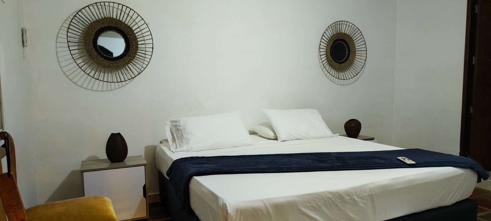 A bedroom with a bed, two nightstands, a chair, and two wall-mounted mirrors.