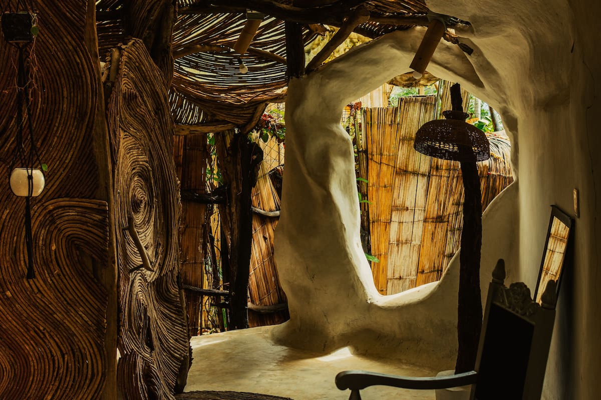 A rustic interior with a unique curved ceiling, a woven chair, and a small window.