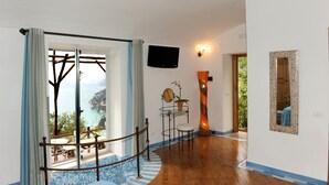 Une chambre avec vue sur la mer, un téléviseur fixé au mur, une horloge et une petite table sur laquelle est posée une plante en pot.