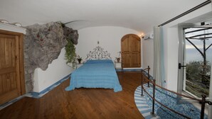 Une chambre à coucher avec un lit, une porte en bois, un mur en pierre et une vue sur l’extérieur.