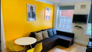 Une pièce avec un mur jaune, un canapé noir, une table blanche et deux chaises jaunes.