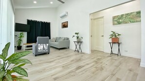 A spacious living room with a grey sofa, a ceiling fan, and two potted plants.
