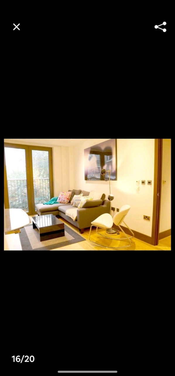 Un salon moderne avec un canapé, une table basse et un fauteuil. Une grande fenêtre offre une vue sur les arbres.