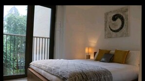 Un dormitorio con cama, mesita de noche, una obra de arte en la pared y vista a zonas verdes.