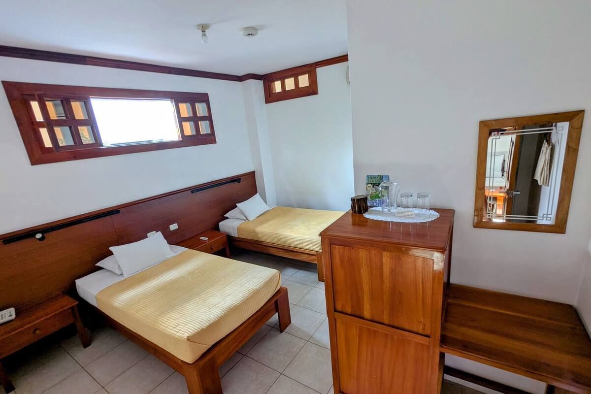 A hotel room with two wooden beds, a wooden nightstand, a wooden desk, and a mirror.