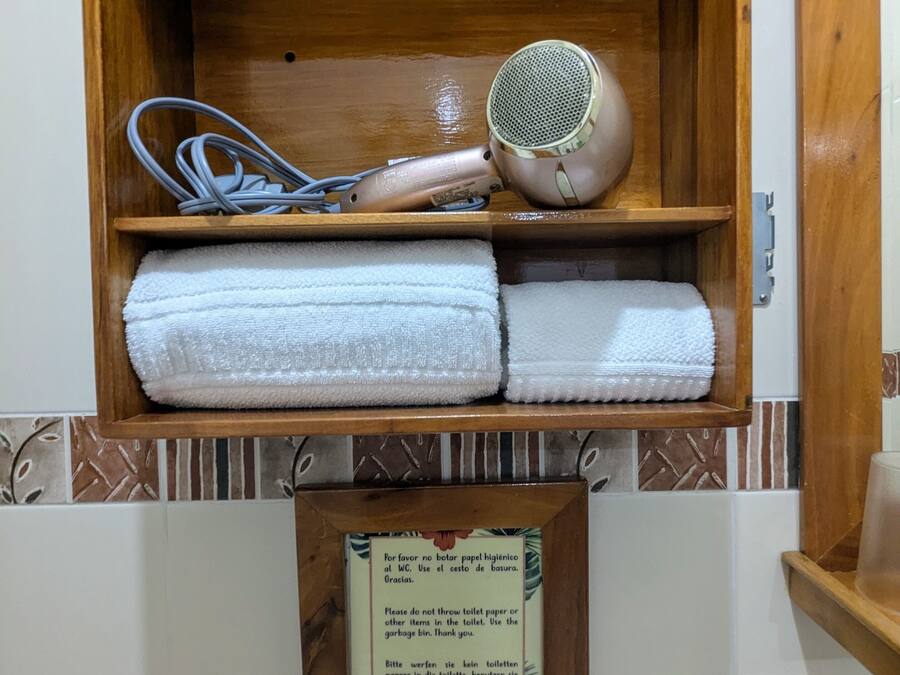 Ein Holzregal mit einem Föhn, Handtüchern und einem Schild, das darauf hinweist, kein Toilettenpapier in die Toilette zu werfen.