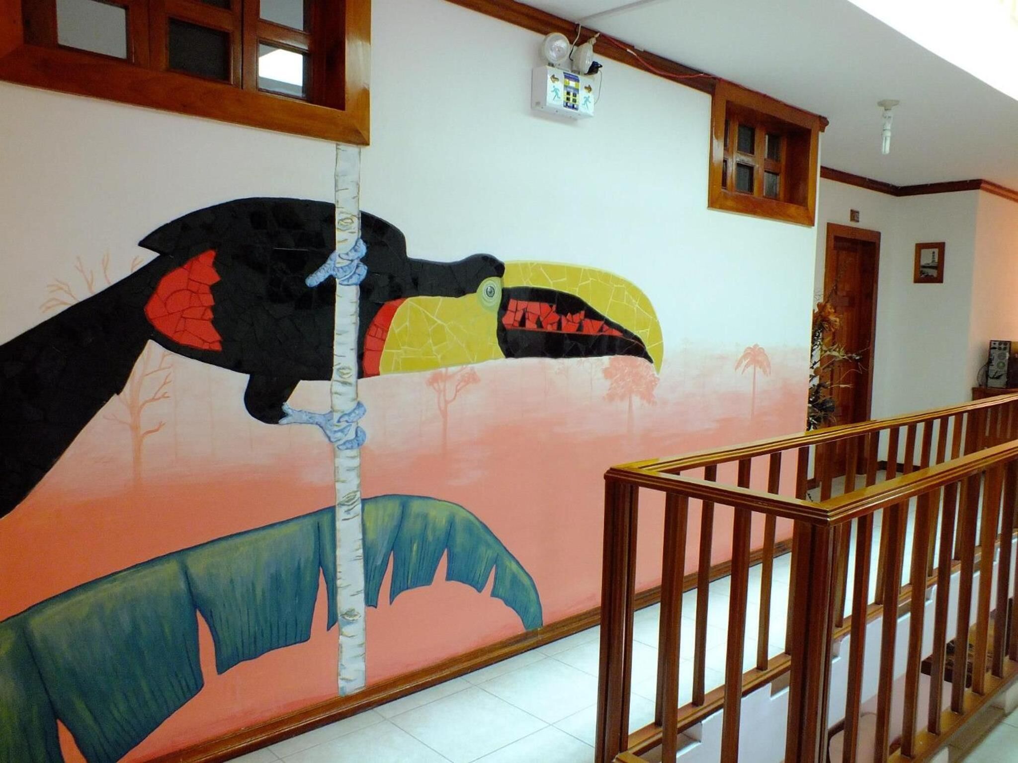 A hallway with a mural of a large bird and a tree, wooden railings, and a ceiling light fixture.