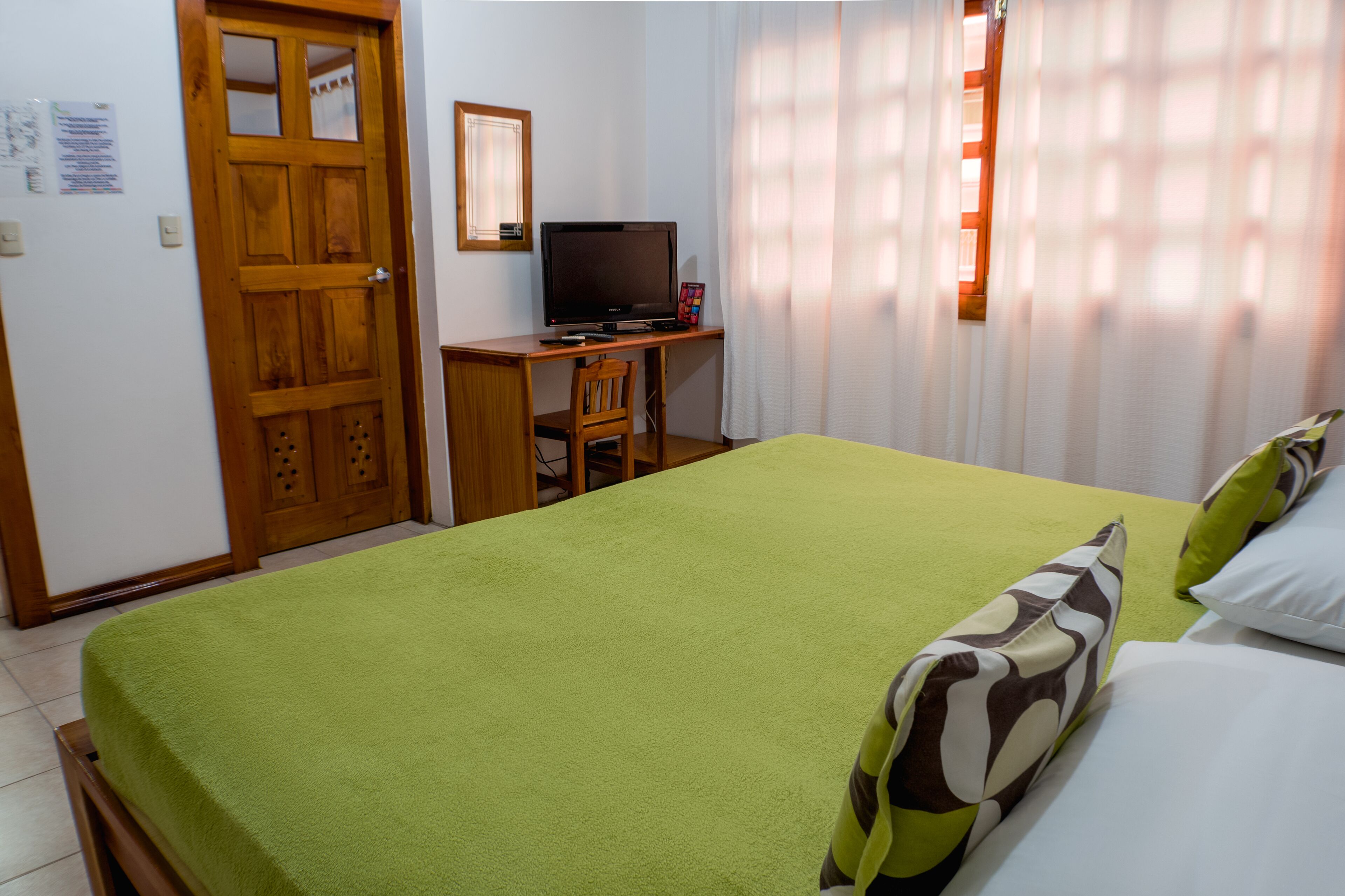 A room with a bed, a desk with a television, and a door.