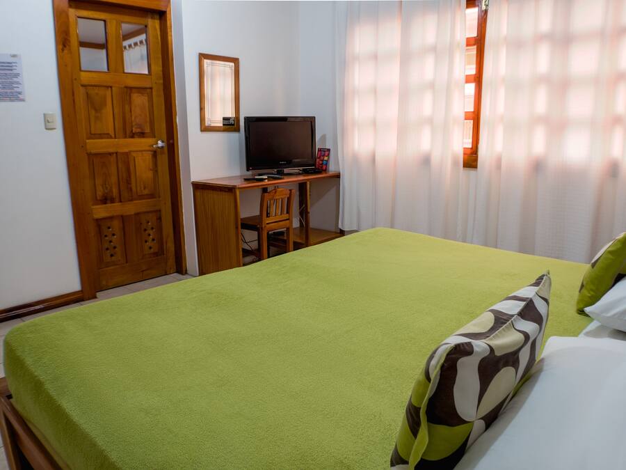 A room with a bed, a desk with a television, and a door.