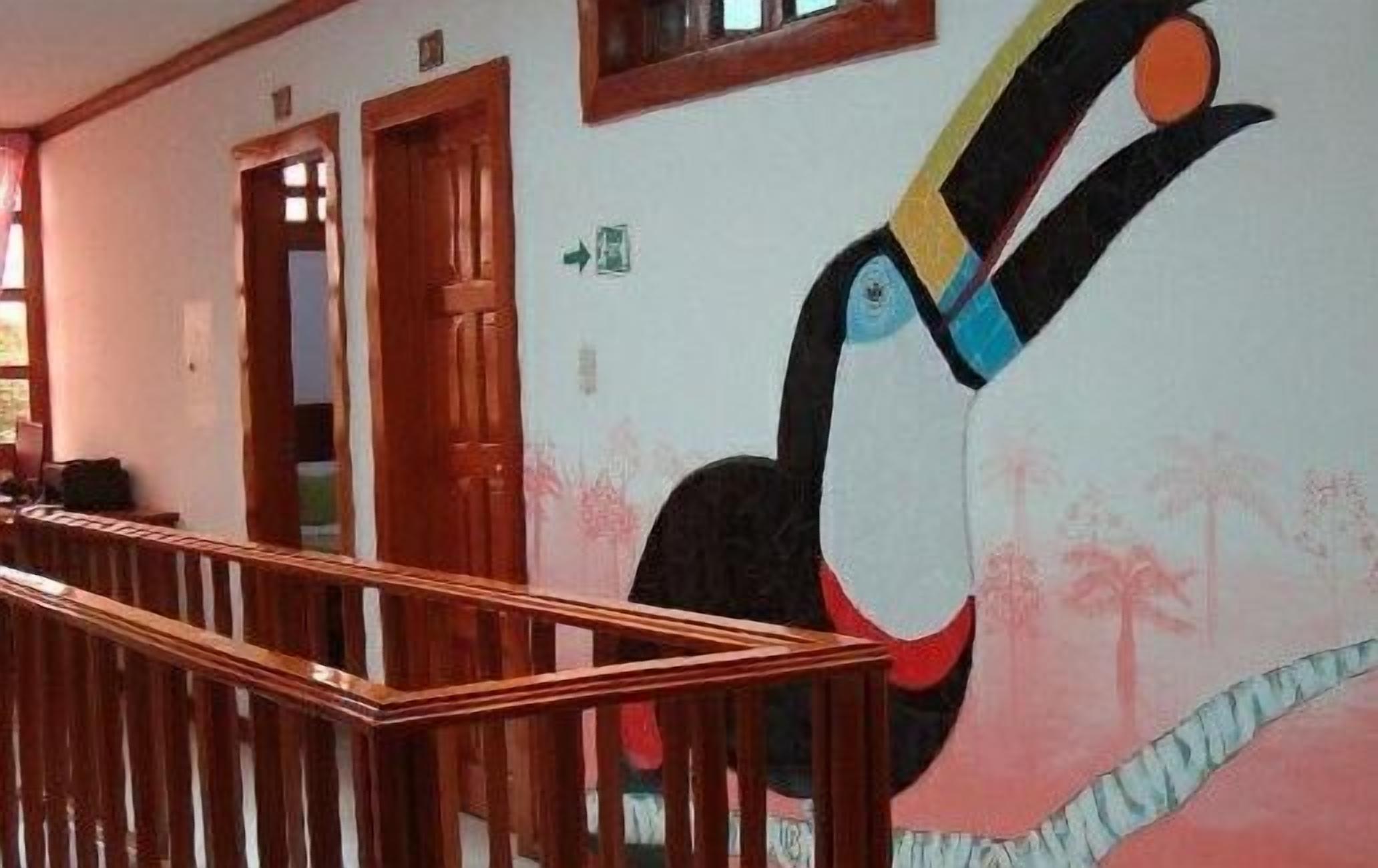 Um corredor com corrimão de madeira, um grande mural de um pássaro e portas que dão para os quartos.
