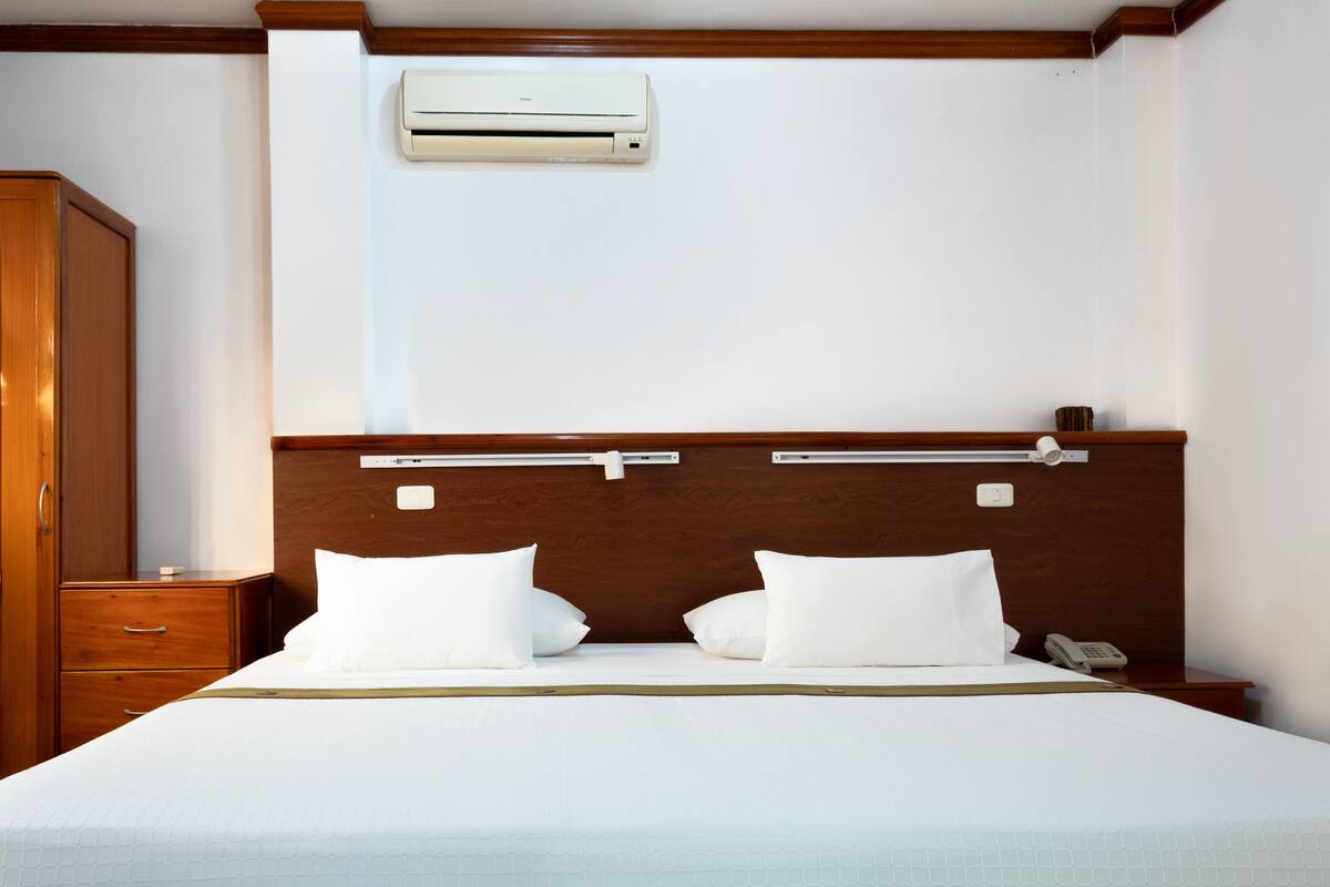 A neatly made bed with white bedding, a wooden headboard, and a bedside table with a phone.