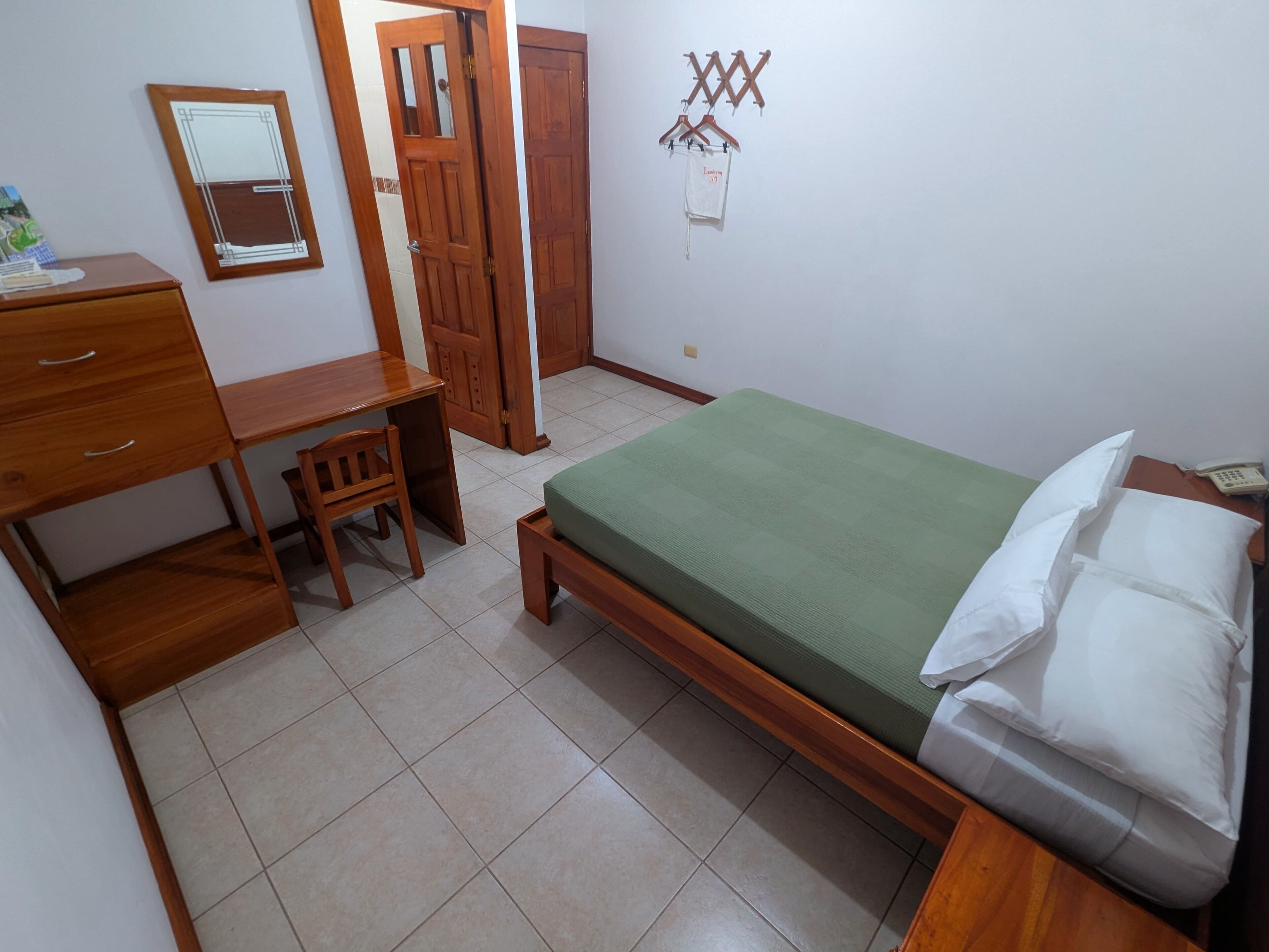 Un dormitorio con escritorio de madera, una silla, una cama con colchón verde y un armario.