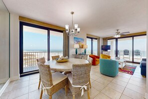 Relax in this stylish living area with a round table, wicker chairs, and a chandelier, offering a view of the beach and ocean.