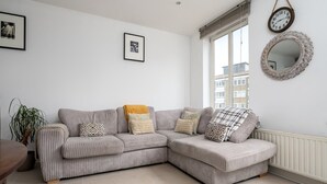 A living room with a grey striped sofa, a round mirror, and two framed pictures on the wall. - GuestReady - Amazing flat in Trendy Hoxton (London)