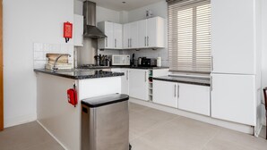 A modern kitchen with white cabinets, a stainless steel range hood, a microwave, and a built-in oven. - GuestReady - Amazing flat in Trendy Hoxton (London)