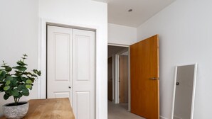 A hallway with a wooden table and a potted plant, white doors, and a tiled floor. - GuestReady - Amazing flat in Trendy Hoxton (London)