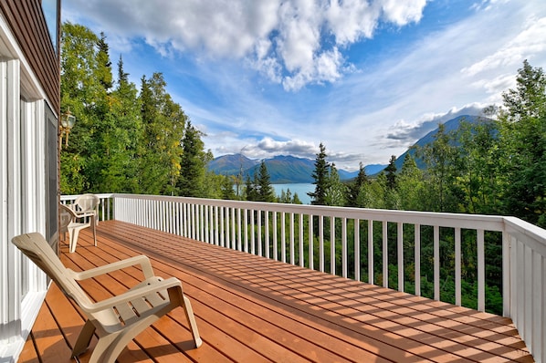 A wooden deck with a white railing, a single beige chair, and a view of mountains and trees.