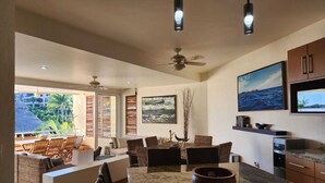 Un vaste espace de vie comprenant une grande table à manger, des sièges confortables, un ventilateur de plafond et une vue sur l’extérieur.
