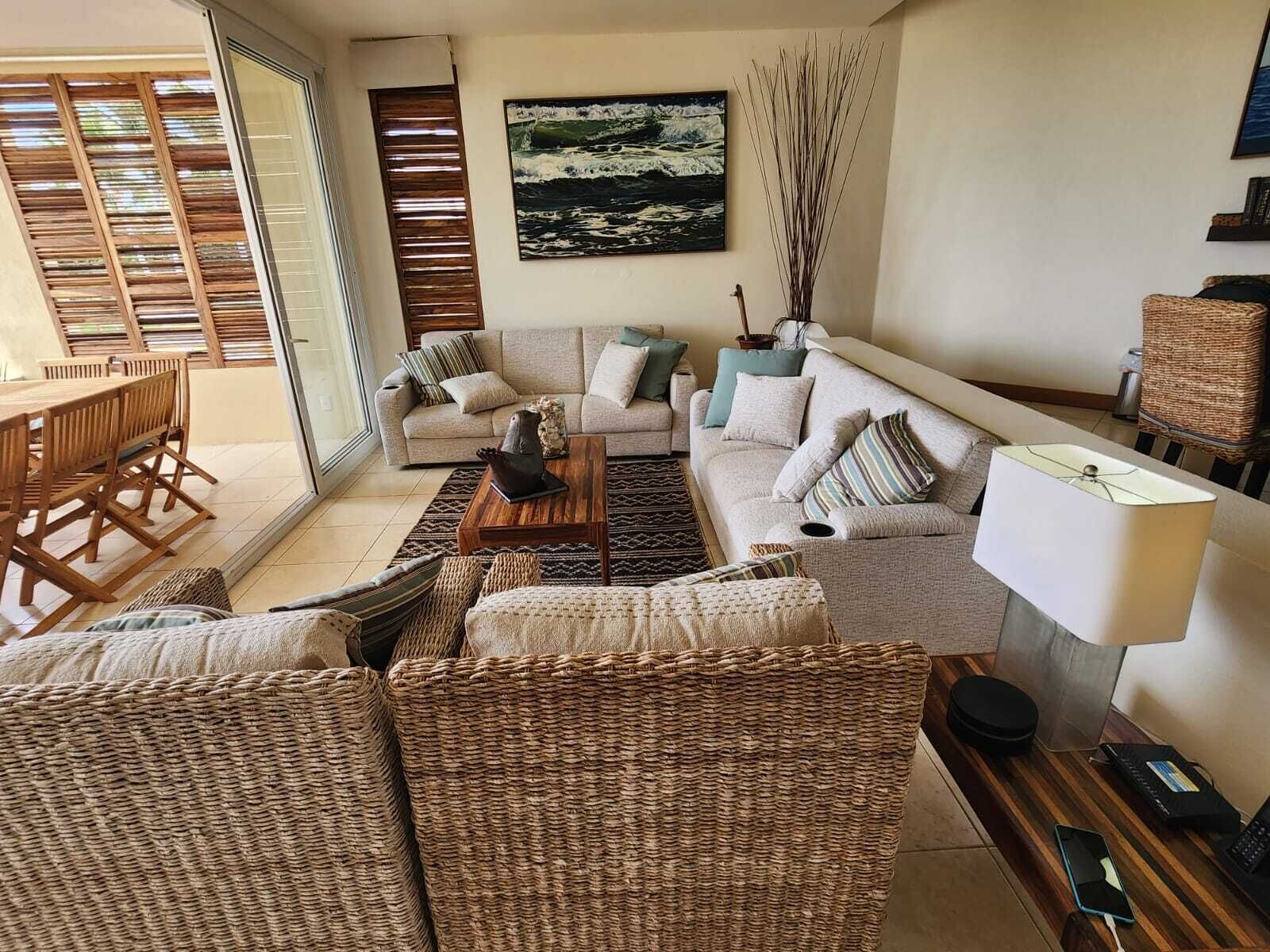 A spacious living room with a sofa set, a coffee table, wicker furniture, and a painting on the wall.