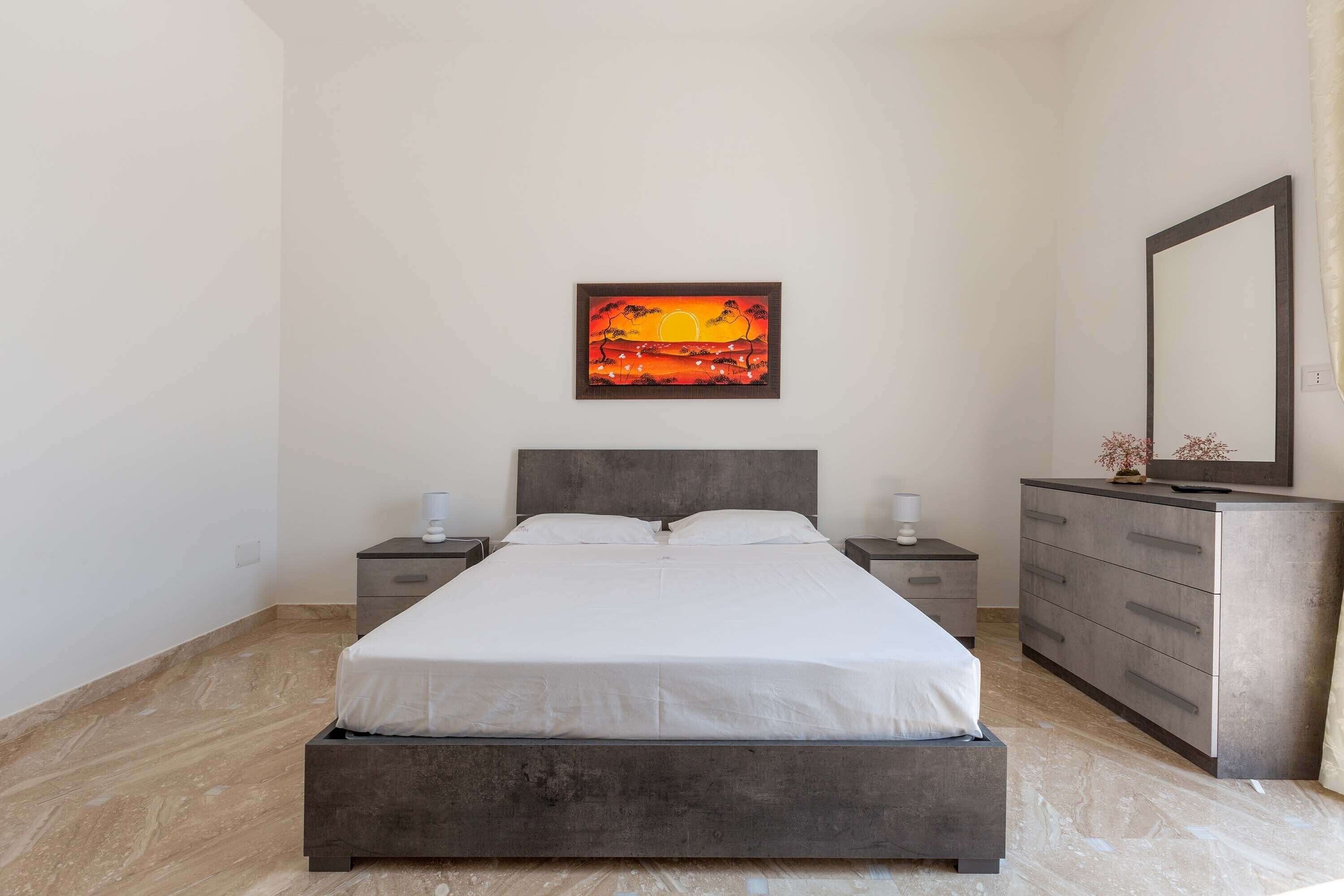 A bedroom with a bed, nightstands, a dresser, and a painting on the wall.