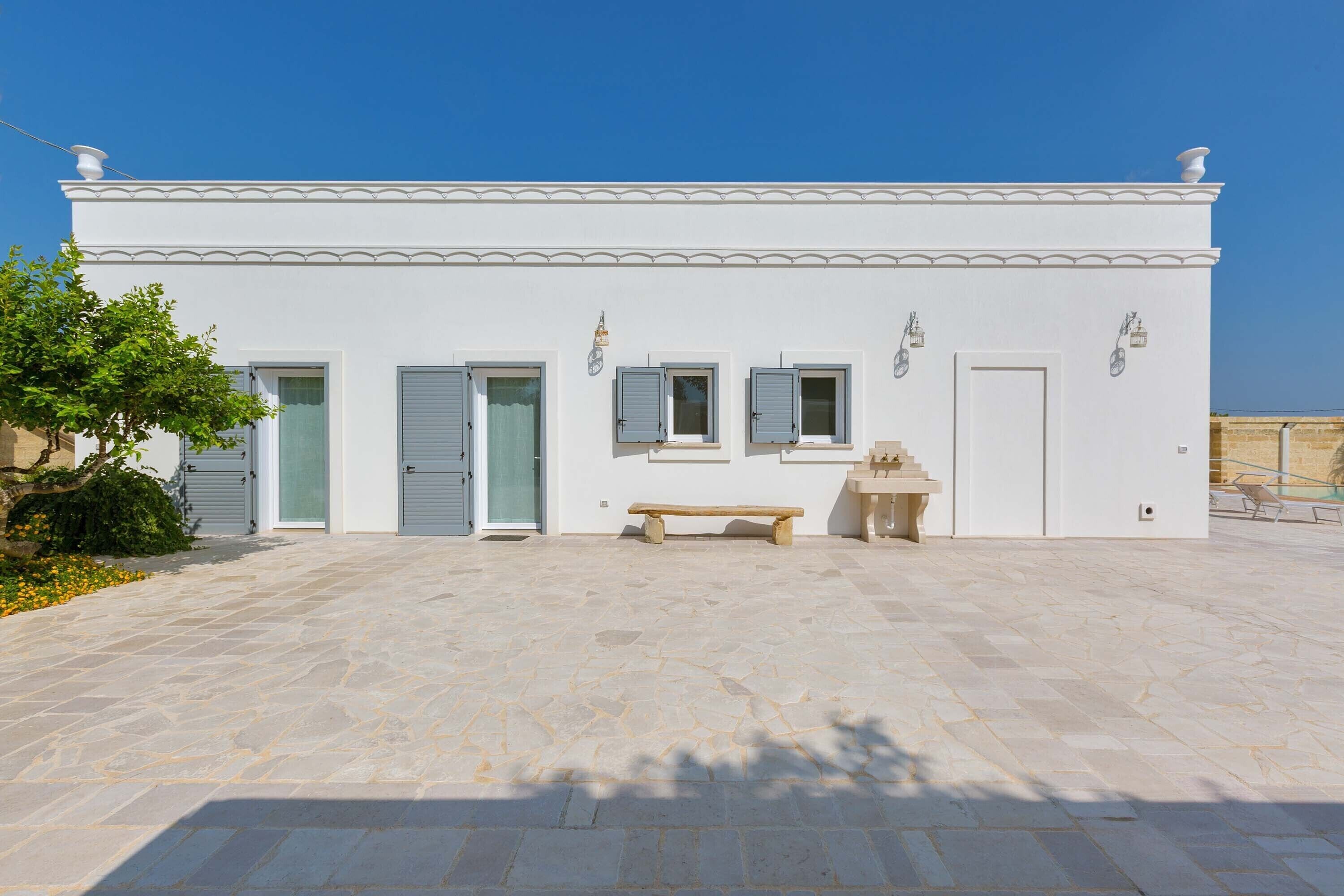 Un edificio blanco con un patio empedrado de piedra, un banco y una pequeña mesa.