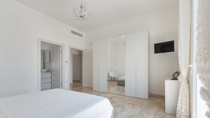 Un dormitorio con cama, armario, televisor y ventana con cortinas.