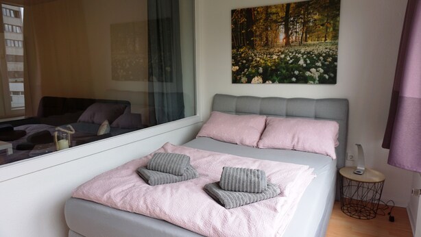 A bedroom with a bed, pillows, a bedside table, a lamp, and a window. - Central location, close to the train station and the fjord, bus stops nearby (Kiel)