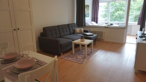 A modern living room with a dark grey sofa, a white coffee table, and a dining area with pink plates and cutlery. - Central location, close to the train station and the fjord, bus stops nearby (Kiel)