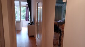 A hallway with a wooden floor, a black doormat, and a door leading to a room with a bed and a window with curtains. - Central location, close to the train station and the fjord, bus stops nearby (Kiel)
