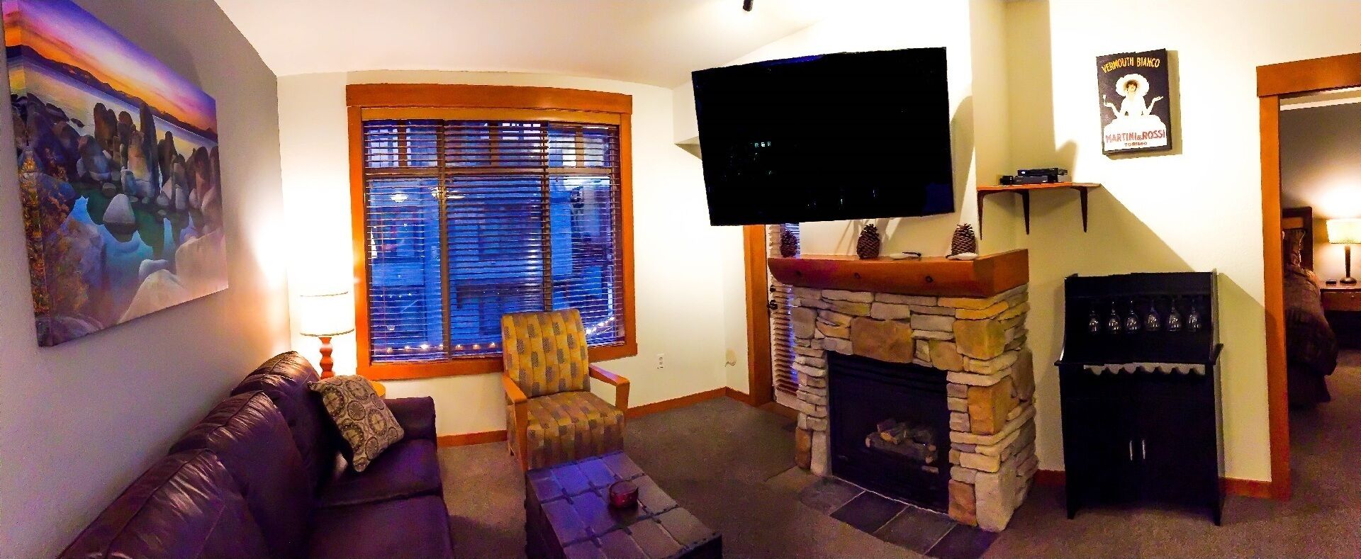 Una sala de estar con chimenea de piedra, un televisor de pantalla plana montado encima, un sofá, un sillón estampado y un cuadro en la pared.