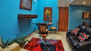 Un salon avec un mur bleu, une table basse en verre, un canapé en cuir noir et un tapis rouge.