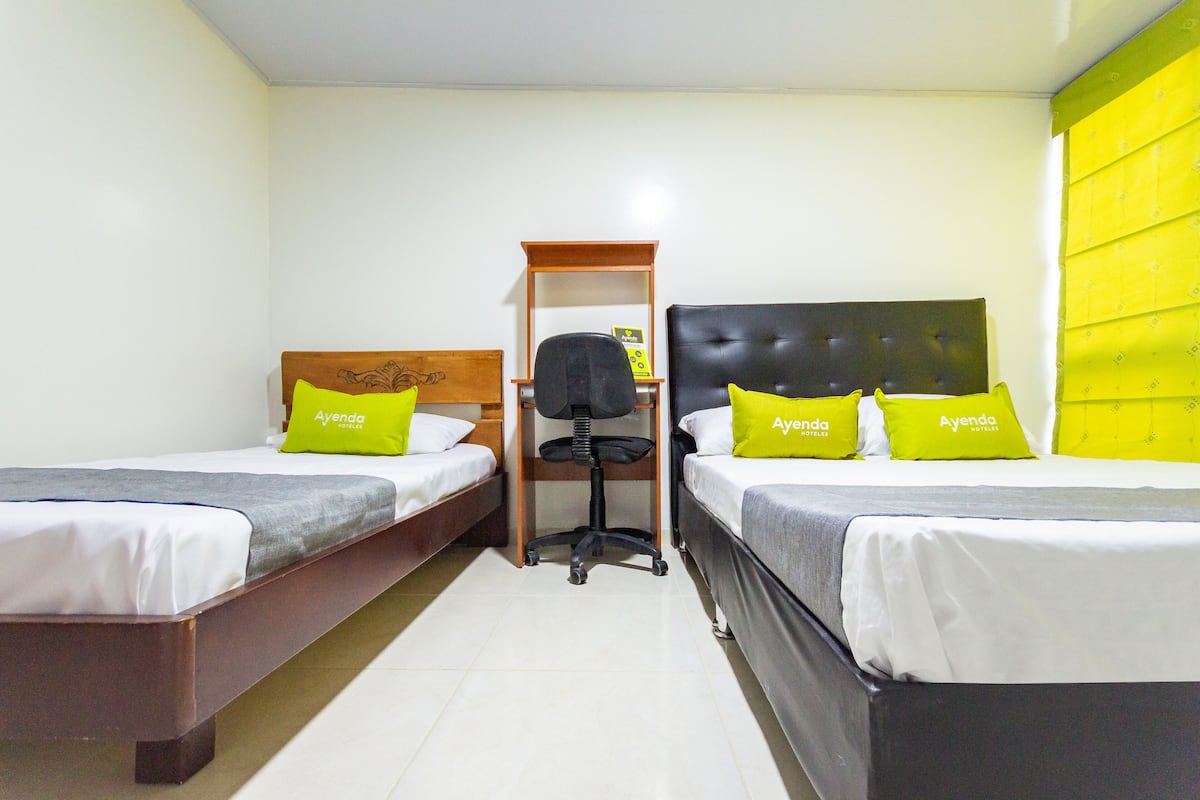 Habitación de hotel con dos camas individuales, una mesita de noche de madera, una silla de oficina negra y una pared de acento amarilla.