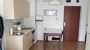 Een kleine leefruimte met een kitchenette, een eethoek en een deur naar een andere kamer.